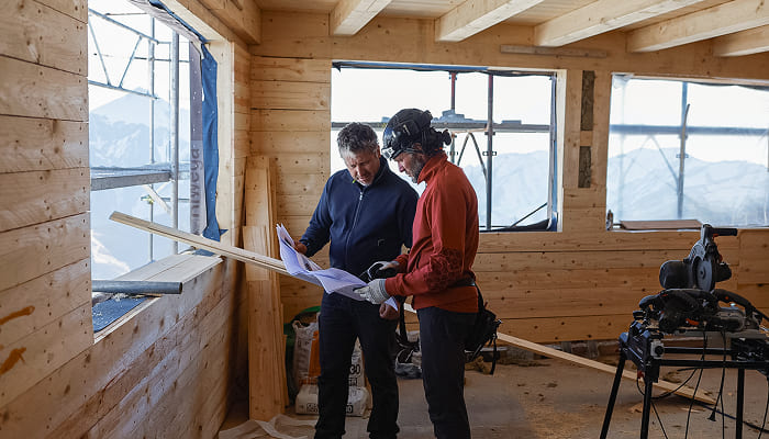 Zwei Handwerker prüfen Pläne auf einer Baustelle.